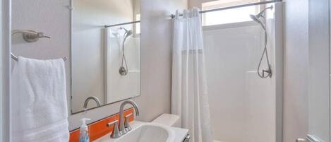 Un baño con lavamanos, espejo, ducha e inodoro.