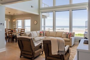 Ein großzügiges Wohnzimmer mit einem großen Fenster mit Blick auf den Strand, einem Essbereich mit einer Kristallleuchter und einer gemütlichen Sitzecke.