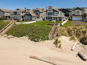 Ein Küstenanwesen mit mehreren Häusern, einem Sandstrand und einer Holztreppe zum Strand.