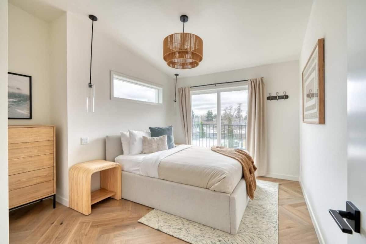 Un dormitorio con cama, mesita de noche, ventana y lámpara colgante.