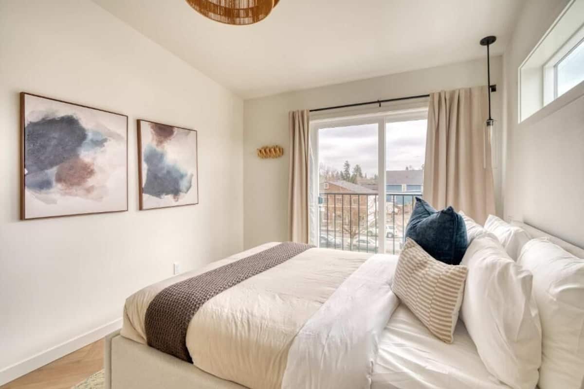 Un dormitorio con cama, ventana con cortinas y dos obras de arte abstractas en la pared.
