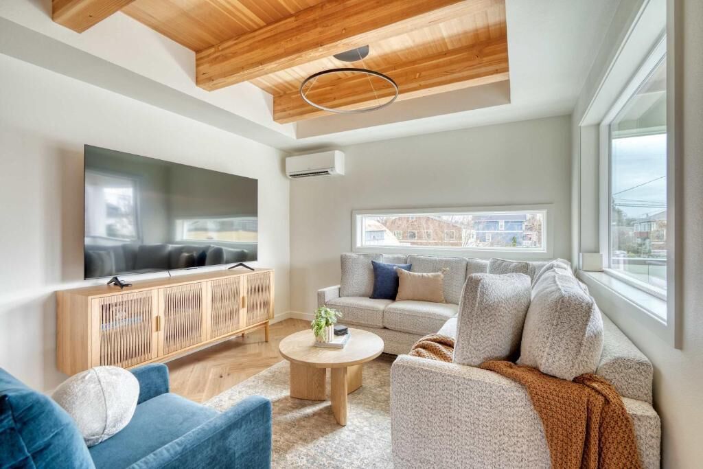 A modern living room with a flat-screen TV, a wooden ceiling, a sofa, a coffee table, and a window with a view.