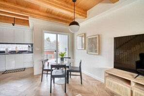 A modern kitchen with white cabinets, a dining area with a round table and chairs, and a large TV on a wooden stand.