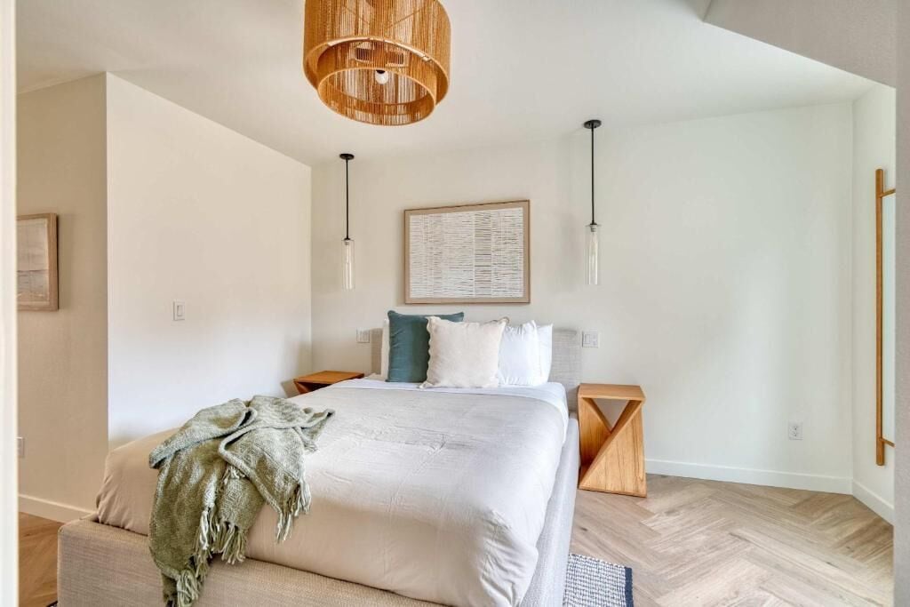 Un dormitorio con una cama grande, una mesita de noche de madera, una lámpara colgante y un cuadro enmarcado en la pared.