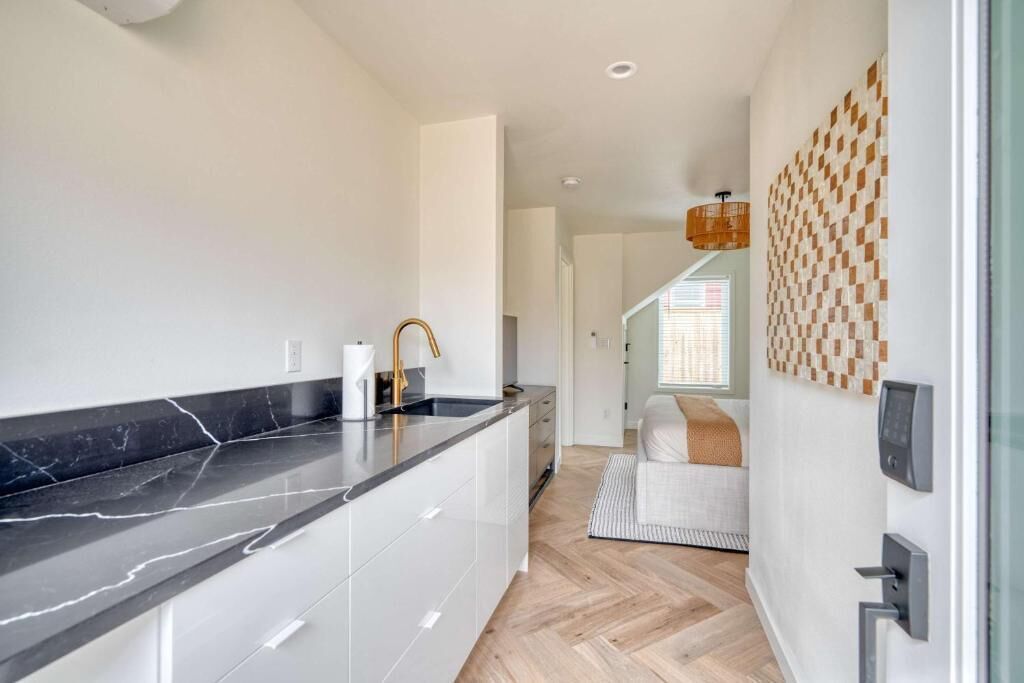 A modern kitchen with a black marble countertop, white cabinets, and a gold faucet.
