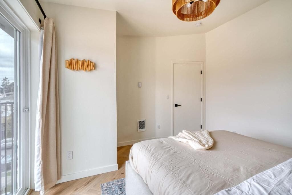 Une chambre à coucher avec un lit, une fenêtre, une porte et un luminaire fixé au mur.