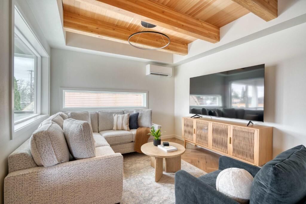 Un salon moderne avec un canapé d’angle, une table basse ronde, un téléviseur et un plafond en bois.