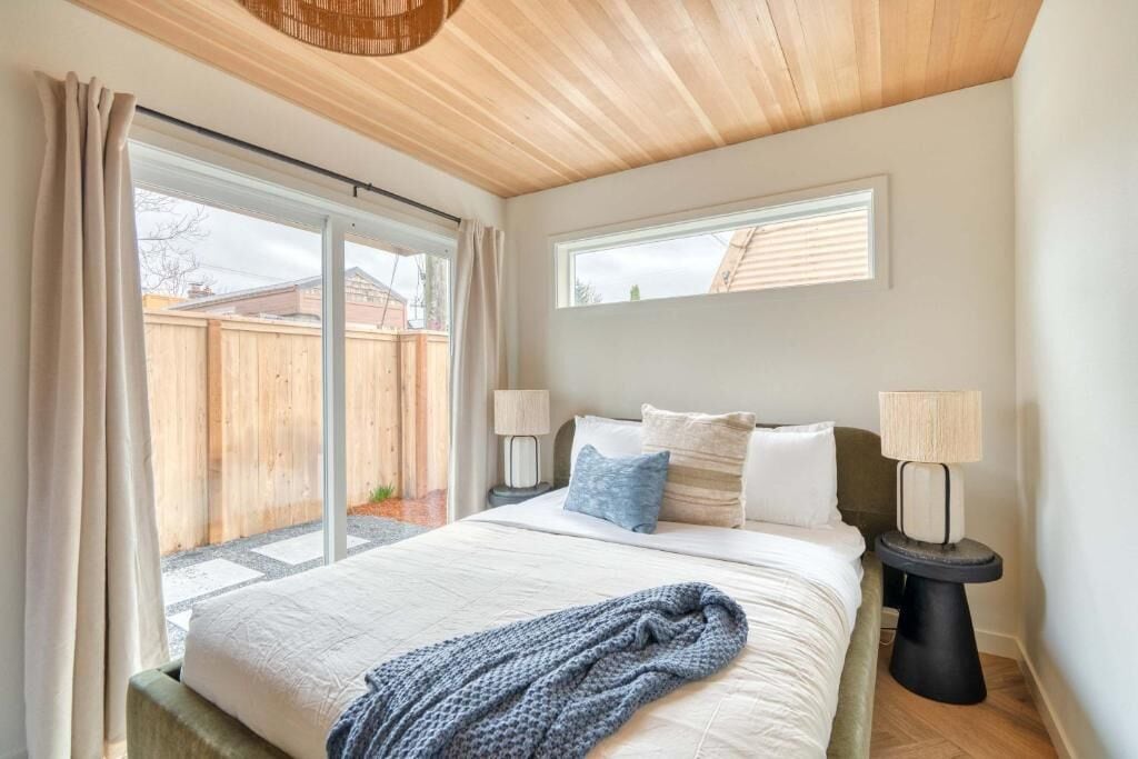 A bedroom with a bed, two bedside lamps, a window, and a view of the outside.