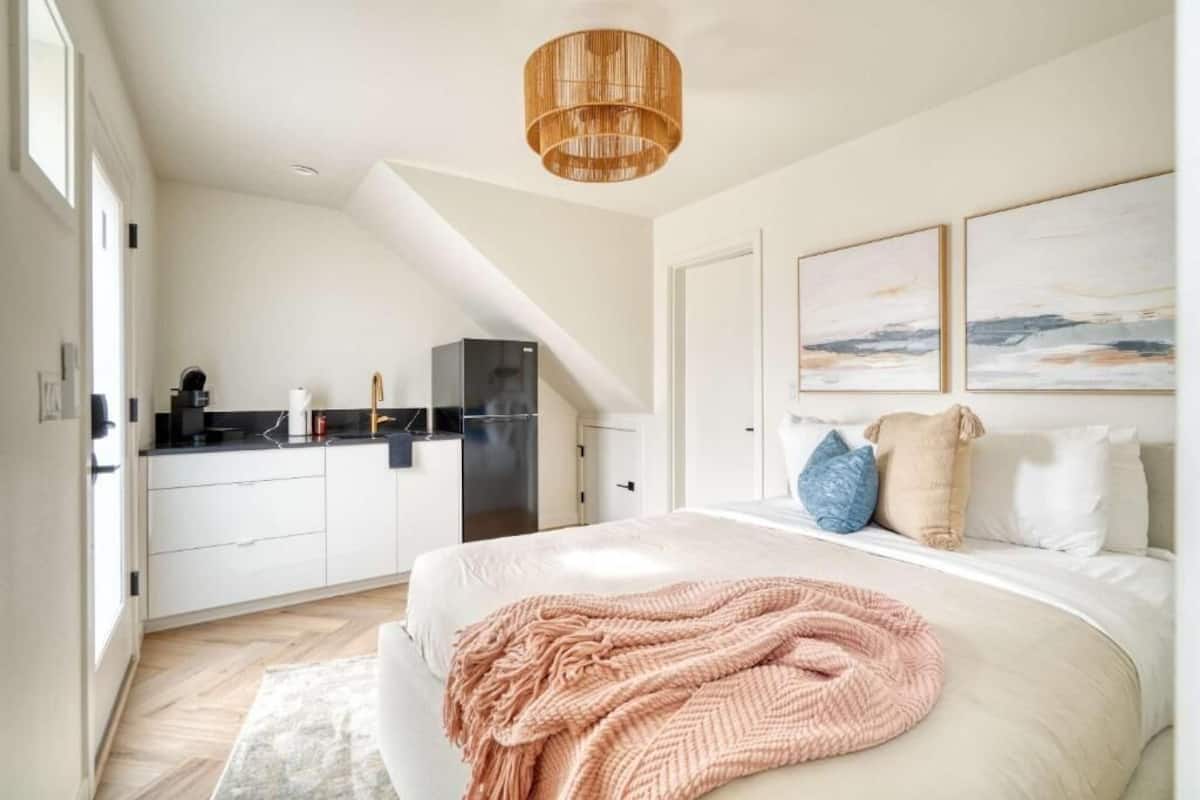 Un dormitorio con cama, mesita de noche, lámpara colgante y vista a la cocina.