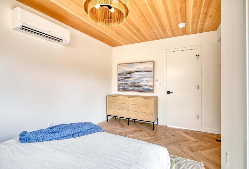 Une chambre à coucher avec un lit, une commode, un tableau et un appareil de climatisation.