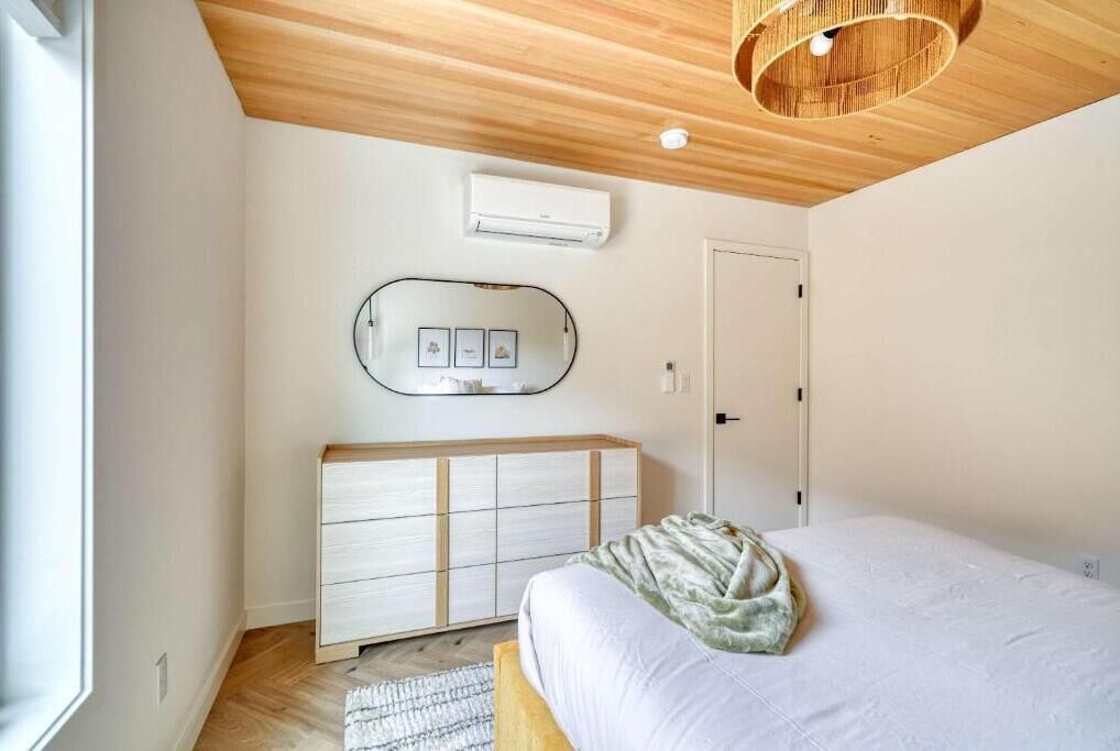 Une chambre à coucher comprenant un lit, une commode, un climatiseur fixé au mur et une porte.