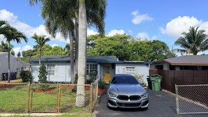 Zona residencial amb una casa, un cotxe aparcat i un pati tancat per una tanca.