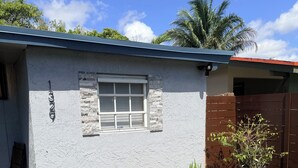 Edifici de planta baixa amb una finestra, una porta i una petita zona de jardí amb plantes.