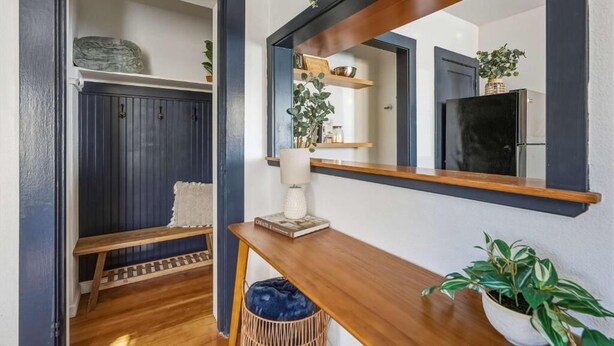 A hallway with a wooden bench, a mirror, a shelf with decorative items, and a potted plant.