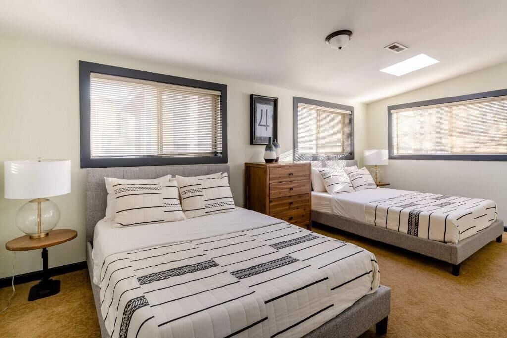 Une chambre avec deux lits, une commode, une lampe et un tableau encadré au mur.