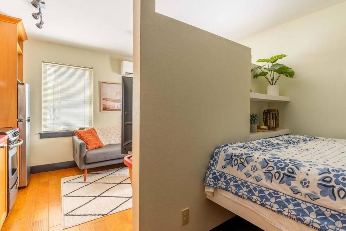 Un dormitorio con cama, ventana, planta y kitchenette.