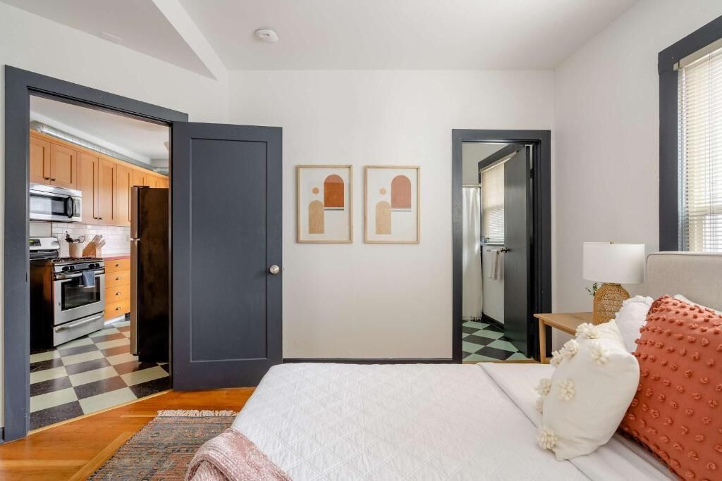 Un dormitorio con cama, mesita de noche, lámpara y vista a la cocina.
