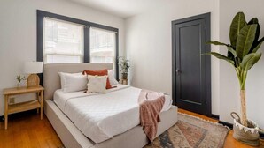 A bedroom with a bed, bedside tables, a door, and a potted plant.