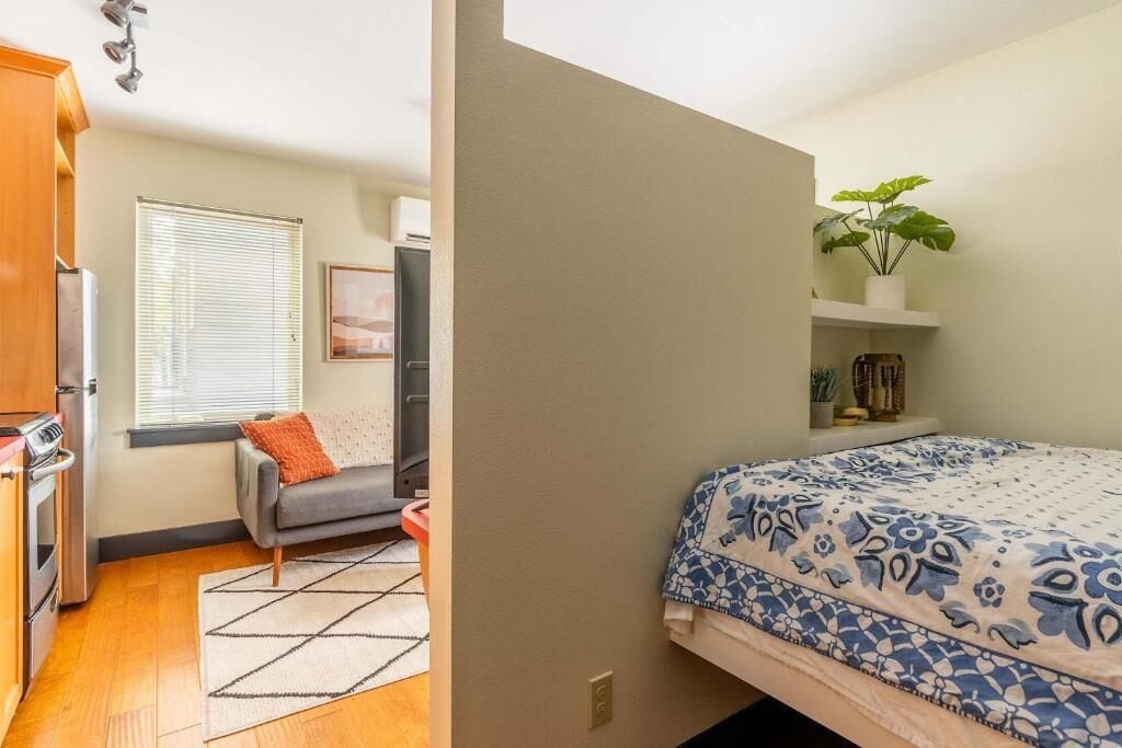 Un dormitorio con cama, ventana, planta y kitchenette.