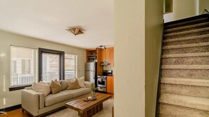 A living room with a sofa, coffee table, and kitchen area with appliances.