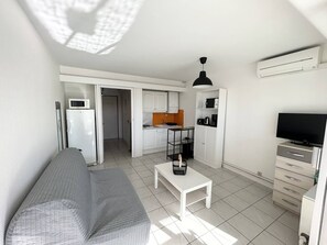 Ein kompakter Wohnbereich mit Küchenzeile, einer Couch, einem Couchtisch, einem Fernseher und einer Deckenleuchte.