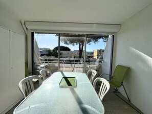 Ein Balkon mit Tisch und Stühlen, Blick auf Gebäude und Bäume, strahlend blauer Himmel.