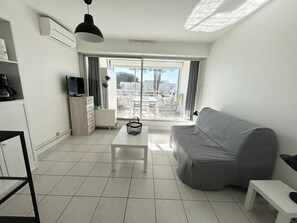 Ein modernes Wohnzimmer mit einer Couch, einem Couchtisch, einem Fernseher und einem Balkon mit Gartenmöbeln.