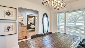 A dining area with a wooden table, a modern chandelier, and a large mirror. - Quiet Furnished 2-Acre Retreat for Medical, Corporate & Family Stays (Manvel)
