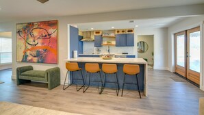 A modern kitchen with a bar area, a green sofa, and a large abstract painting. - Quiet Furnished 2-Acre Retreat for Medical, Corporate & Family Stays (Manvel)