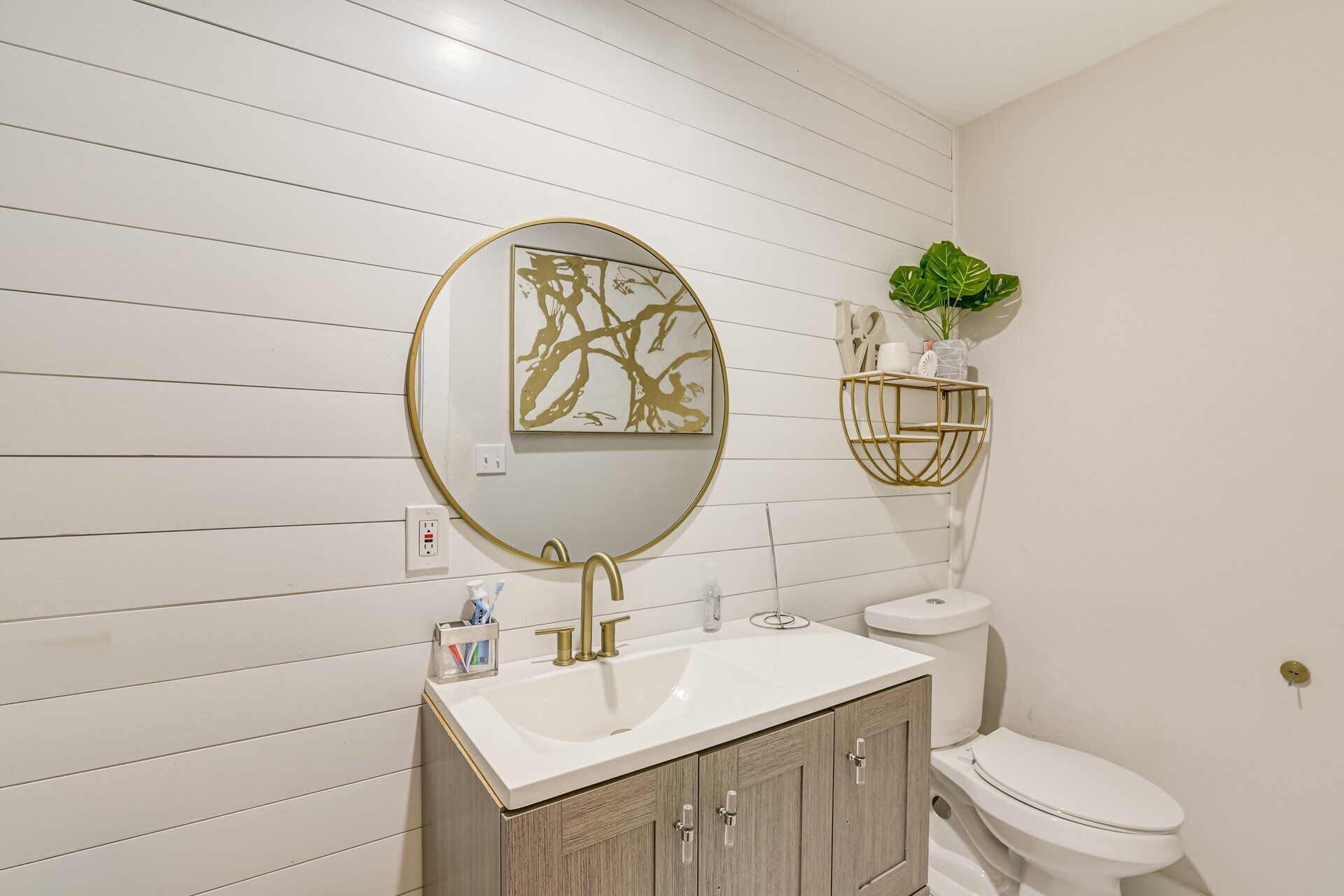 A bathroom with a white sink, gold faucets, a gold-framed mirror, and a toilet with a white tank.