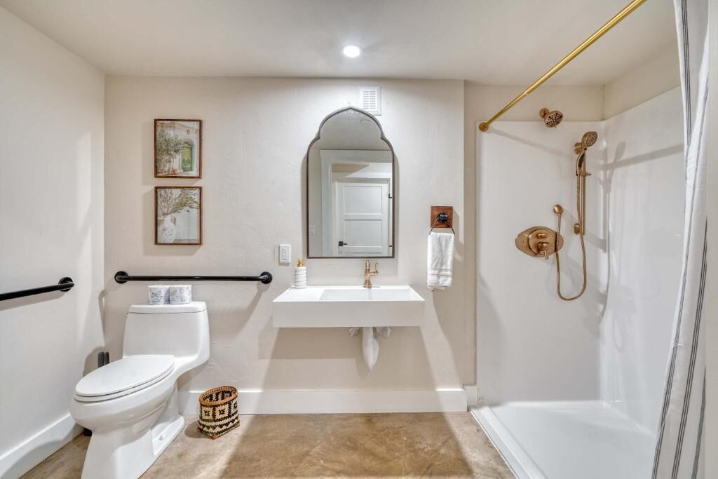 Un baño con inodoro, lavamanos, espejo, ducha y barandilla.
