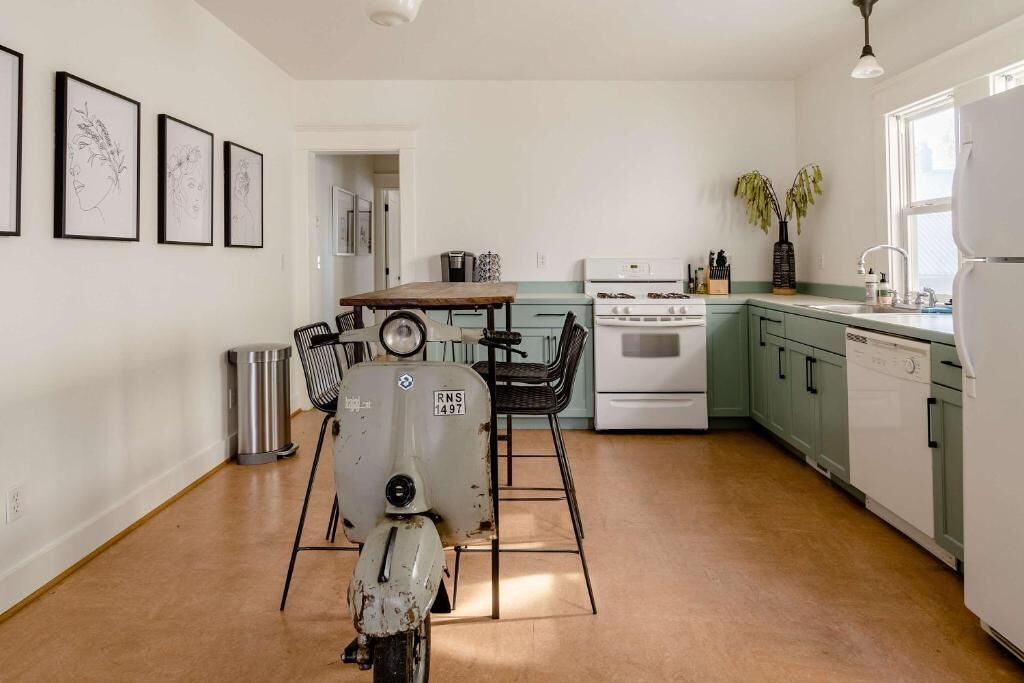 A kitchen with a dining table, chairs, a vintage refrigerator, a stove, and a dishwasher.
