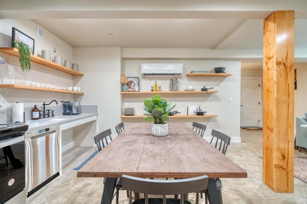 Una cocina moderna con estantes de madera, una mesa de comedor, sillas y un lavavajillas.