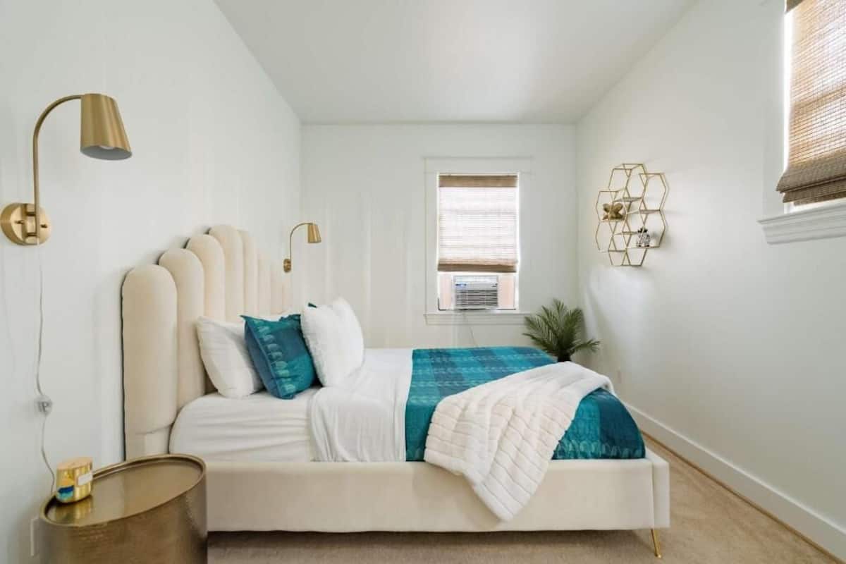 A bedroom with a bed, bedside lamps, a window, and a wall-mounted light fixture.