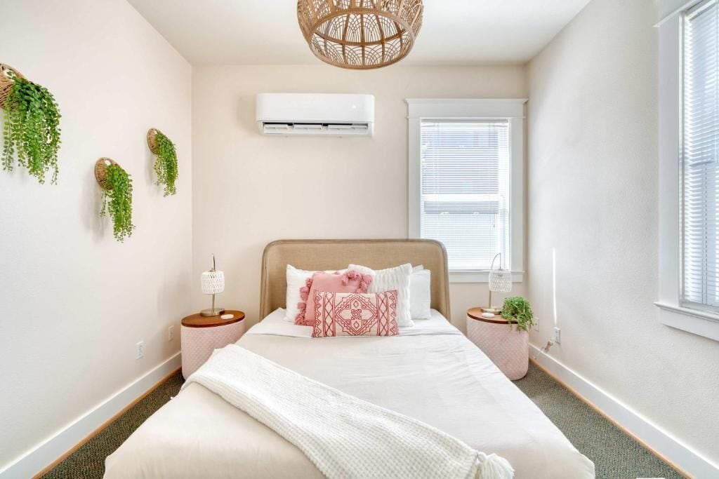 A bedroom with a bed, bedside tables, a window, an air conditioner, and wall-mounted plants.
