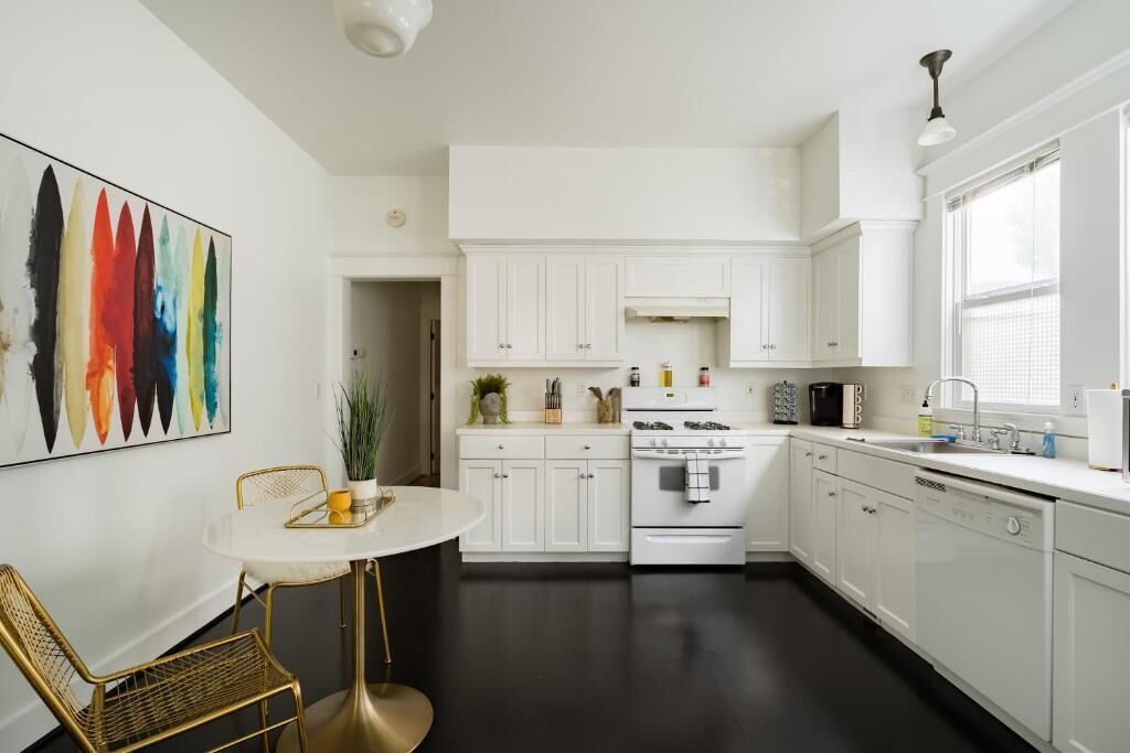 Een moderne keuken met witte kasten, een fornuis en een eethoek met een ronde tafel en stoelen.
