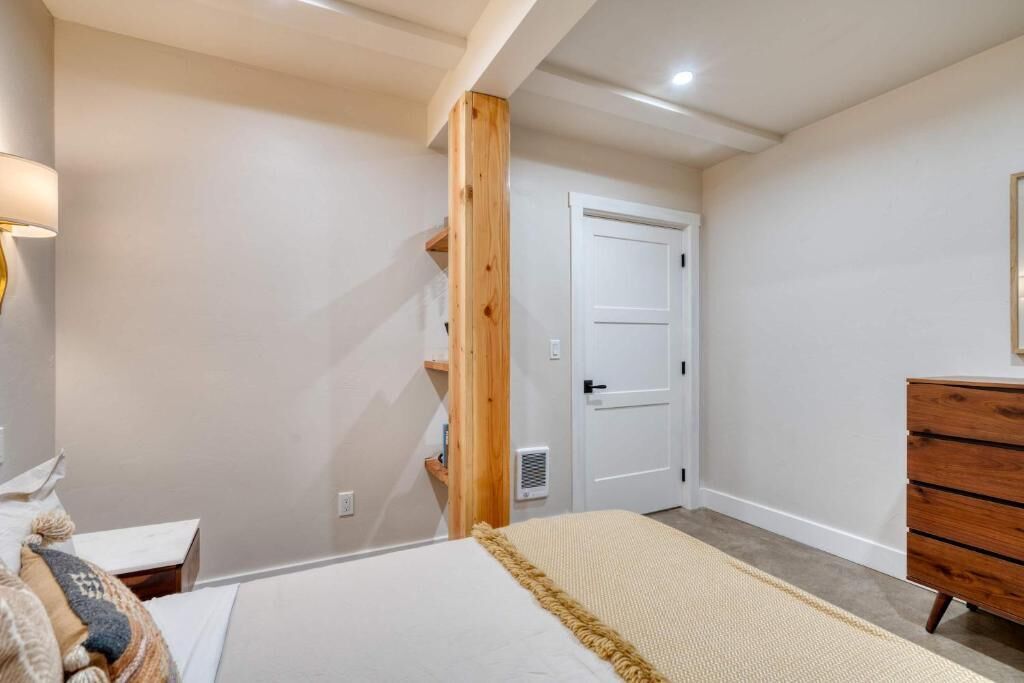 A bedroom with a bed, a wooden shelf, a dresser, and a door.