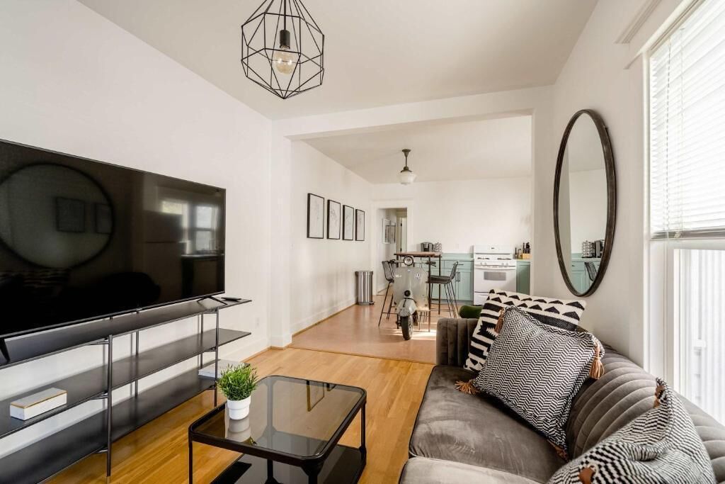 A modern living room with a flat-screen TV, a sofa, a coffee table, and a dining area in the background.