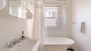 A bathroom with a bathtub, a sink, a mirror, and a window with a view.