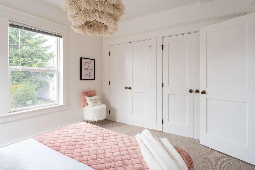 A bedroom with a bed, a window, a door, and a wall-mounted picture.