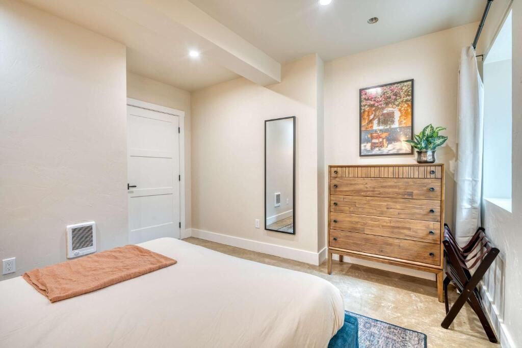 A bedroom with a bed, a wooden dresser, a mirror, and a window with curtains.
