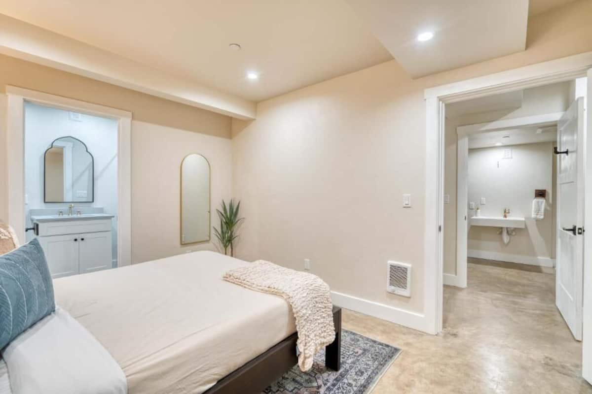 A bedroom with a bed, a bedside table, a mirror, and a bathroom visible through an open door.