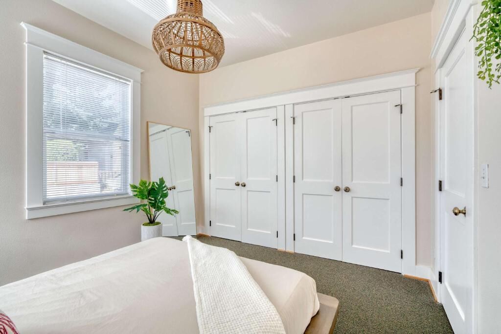 A bedroom with a bed, a large wardrobe, a hanging light fixture, and a window with blinds.