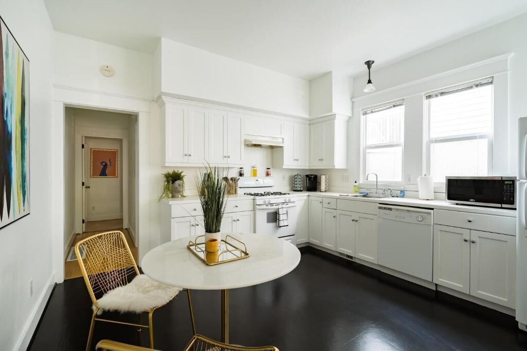 A modern kitchen with white cabinets, a round dining table, and a black floor.