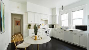 A modern kitchen with white cabinets, a round dining table, and a black floor.