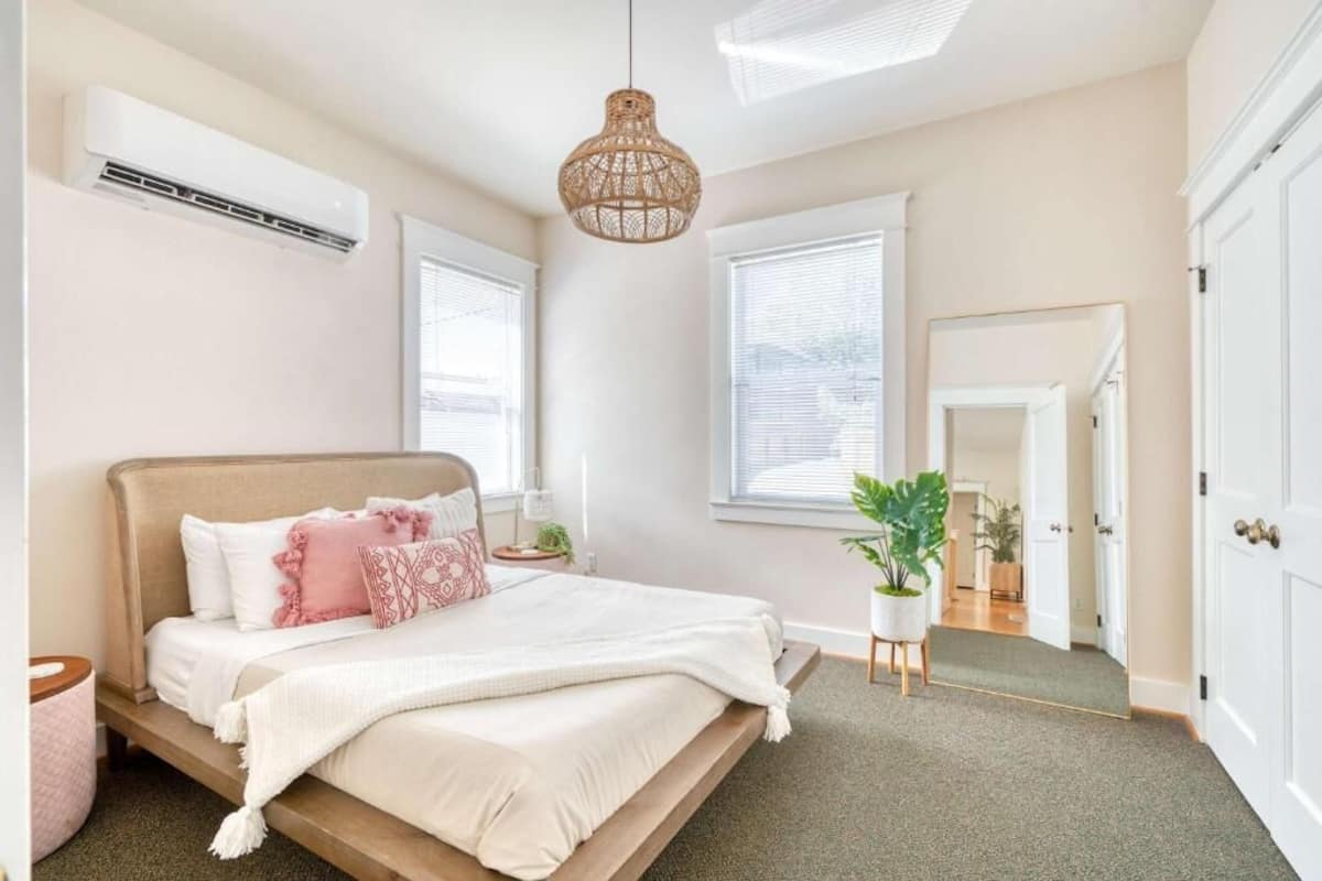 A bedroom with a bed, bedside tables, a hanging light fixture, and a potted plant.