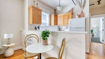 A kitchen with wooden cabinets, a white refrigerator, a marble table, and two chairs.