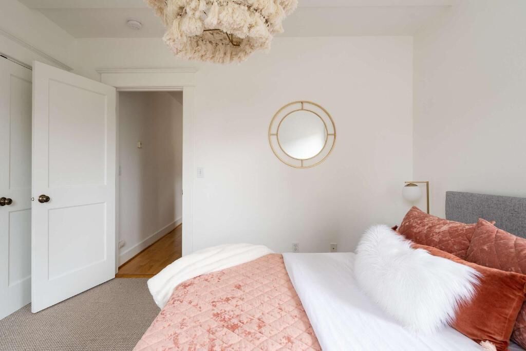 A bedroom with a bed, a round mirror, a door, and a light fixture.