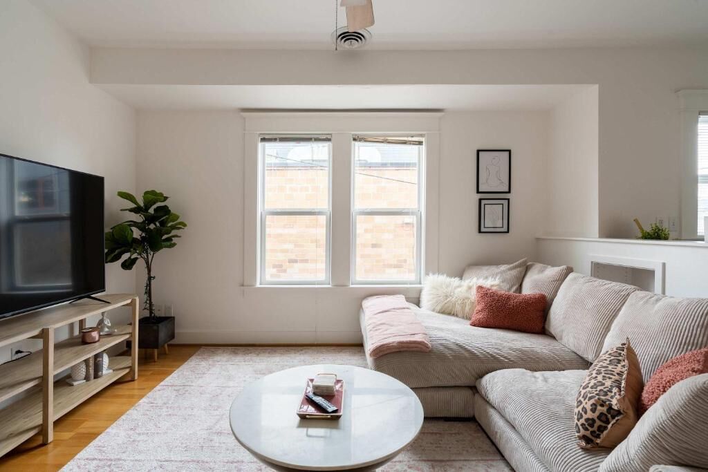 A living room with a TV, sofa, coffee table, and windows.