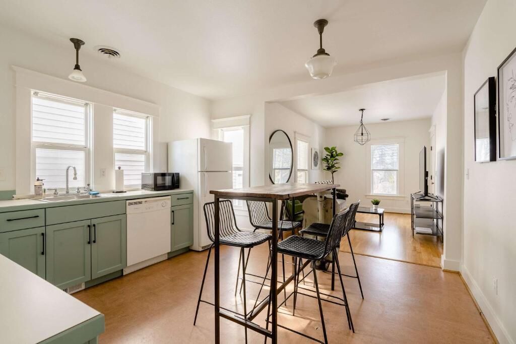 A modern kitchen with a dining area, featuring a wooden table and chairs, a refrigerator, and a sink.